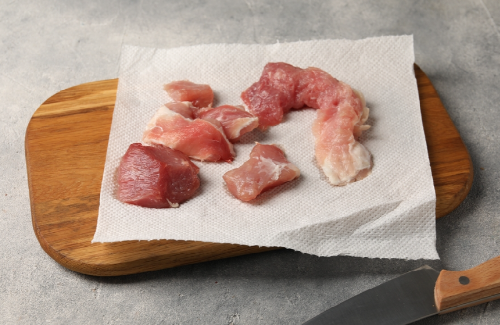 Paper towel, pieces of meat and knife on grey table