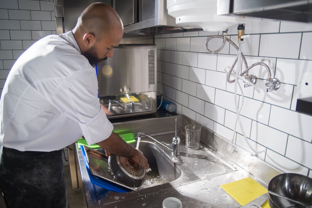 A Man Washing the Frying Pan on the Sink