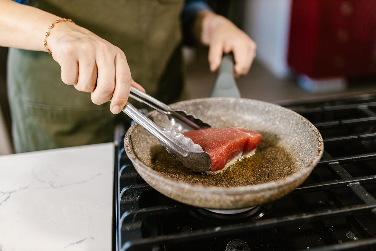 Cook Frying Slice of Red Meat on Gas Cooker