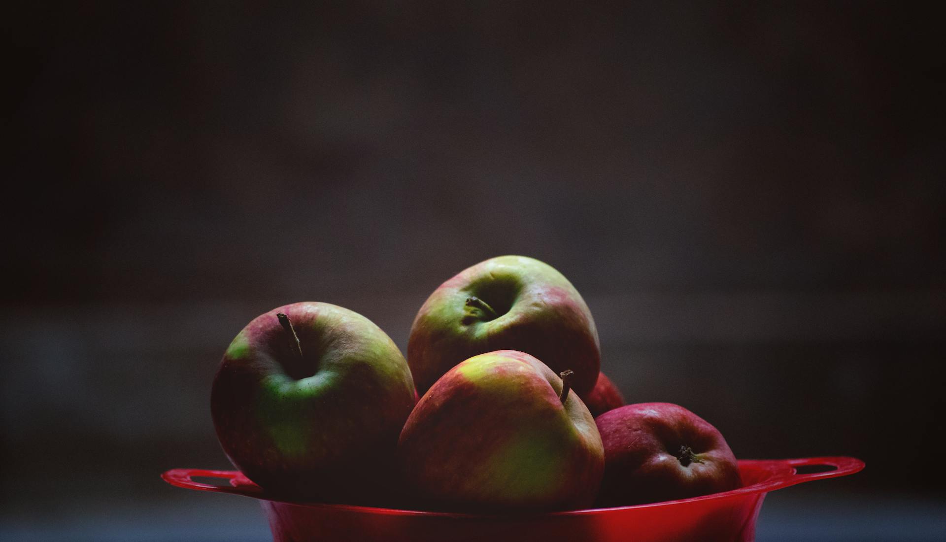 Green and red apples in a red bowl
