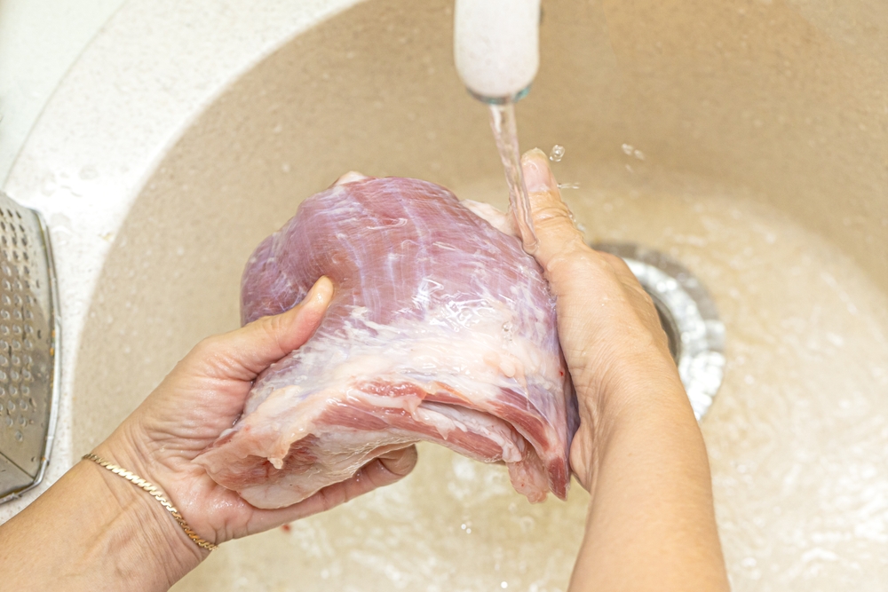 Women's hands wash and clean meat at the kitchen sink