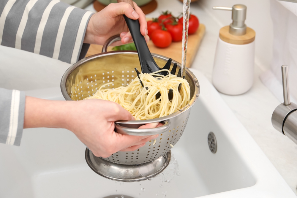 Woman rinsing pasta in colander above sink, closeup