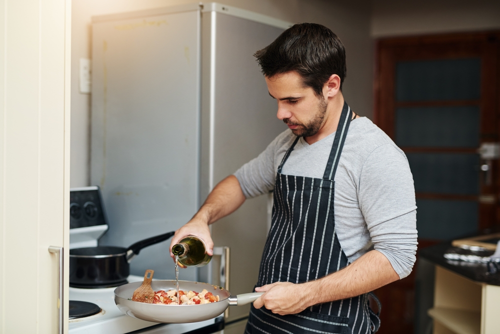 Man cooking food for dinner on kitchen counter with wine.