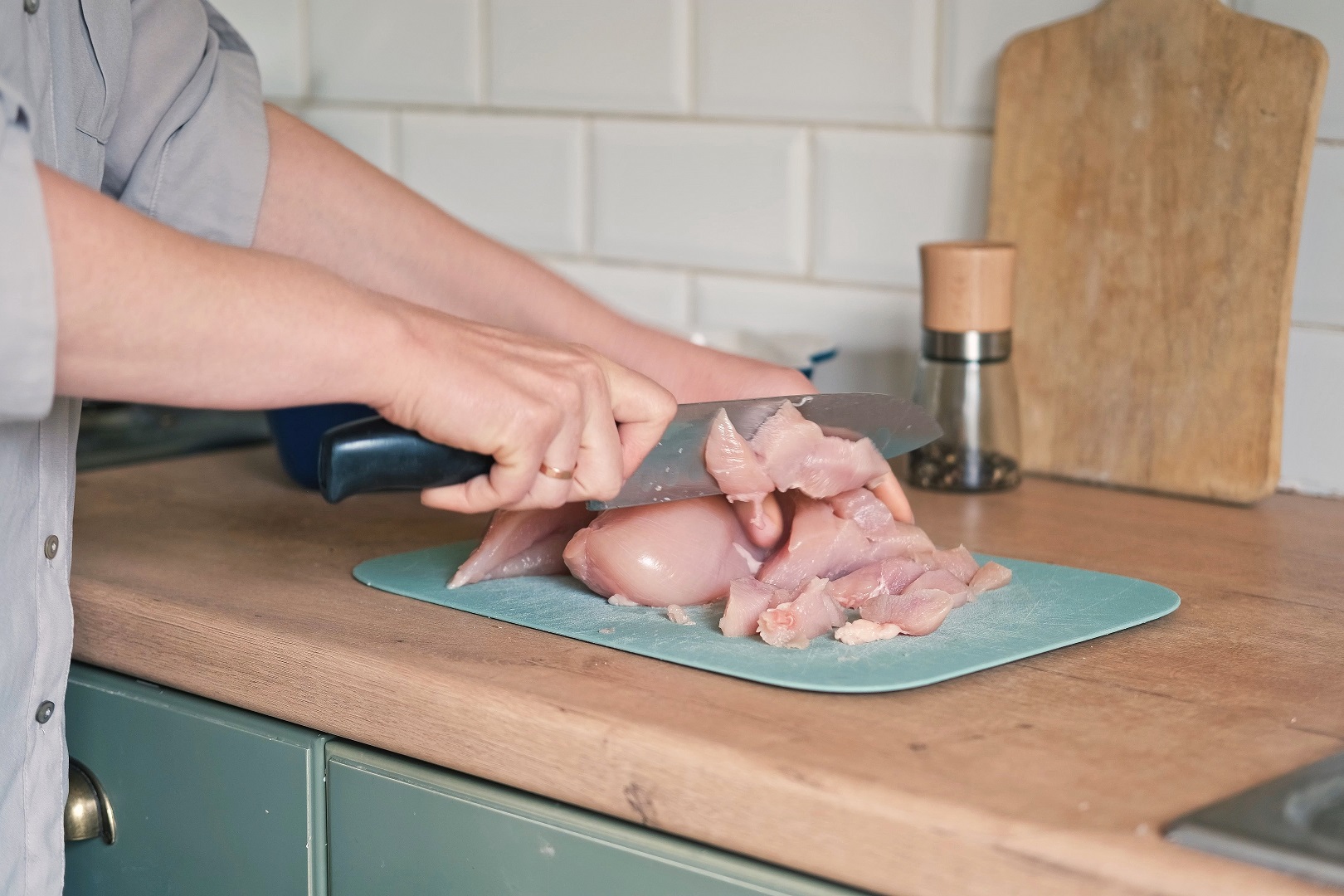 Woman cutting the chicken fillet in pieces for cooking.