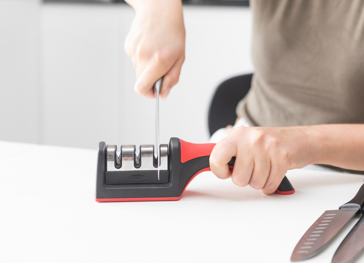 Close-up of woman sharpening knife with special knife sharpener at home