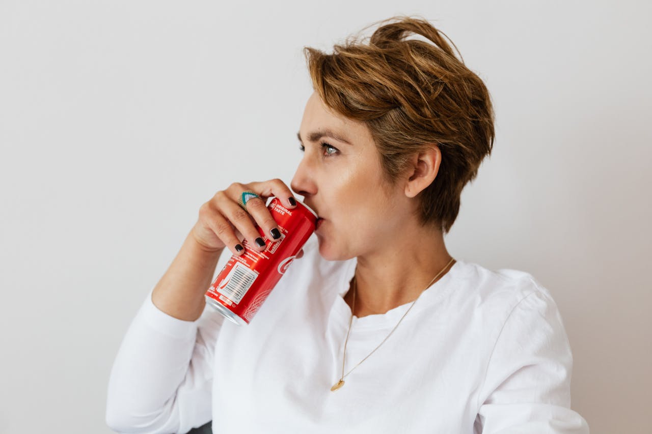 Thoughtful woman drinking coke near white wall