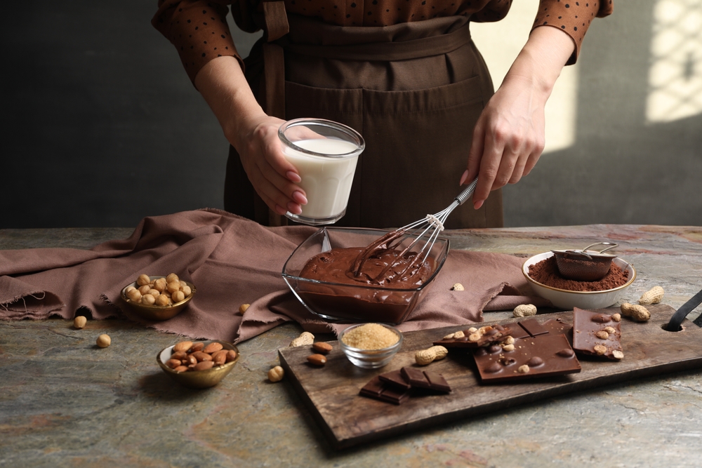 Woman with glass of milk and whisk mixing delicious chocolate cream
