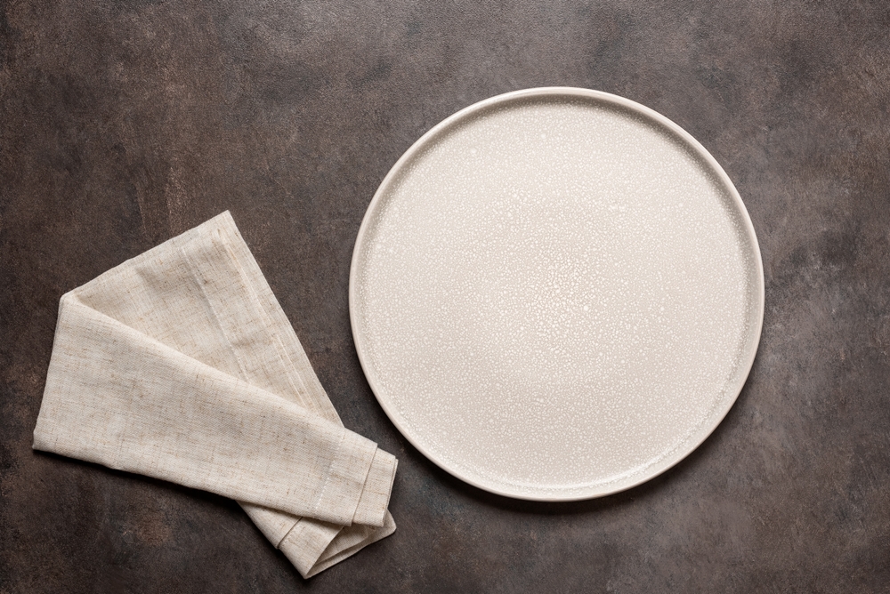Empty beige plate with beige linen napkin on a dark brown background