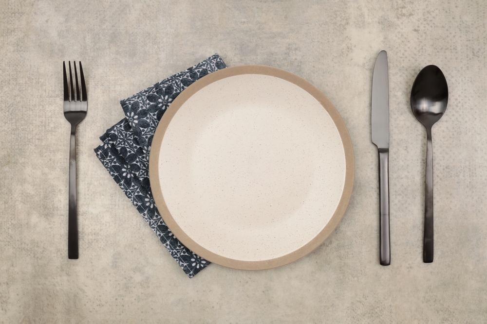 Empty plate, fork; knife, spoon, napkin on marble rustic concrete background.