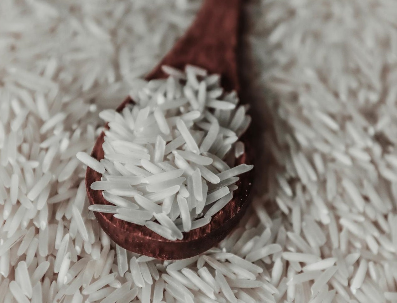 Wooden spoon with rice grains in heap.