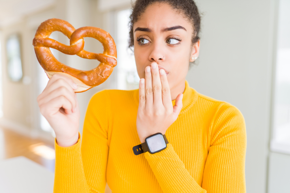 Woman holding German salty pastry pretzel with covered mouth with hand