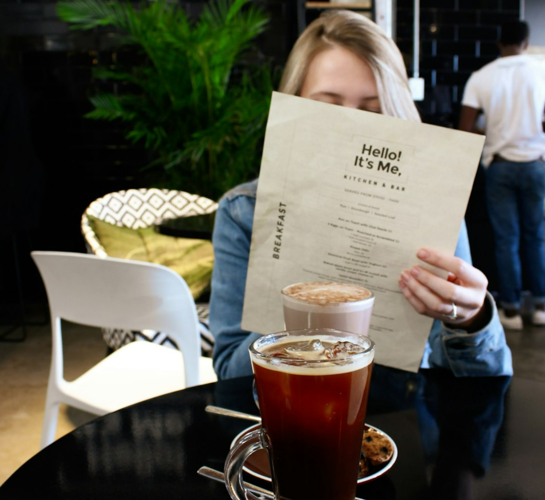woman reading in paper siting beside table with drinks