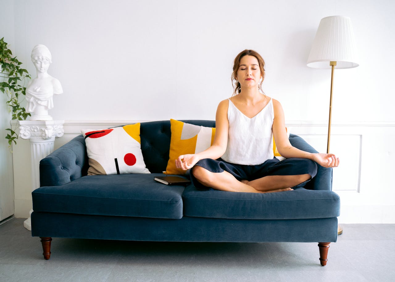 Photo of Woman in a white shirt top and black pants Sitting on a Blue Sofa Meditating