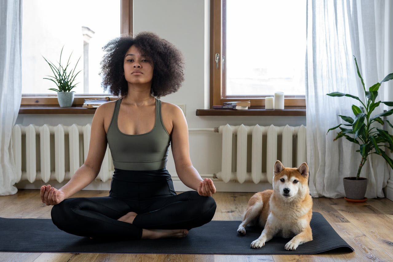 Photo of Woman in Green tank top and Black Pants Sitting on Floor next to a dog Meditating