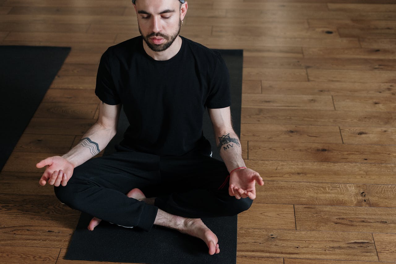 Man in Black Crew Neck T-shirt and Black Pants Sitting on Brown Wooden Floor