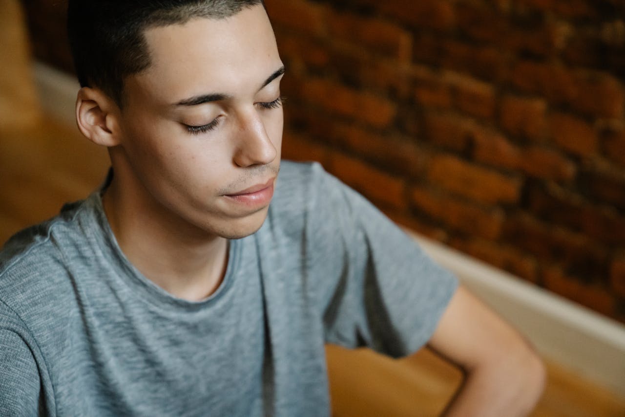 Photo of Man in Gray T-shirt and Sitting on Wooden Floor Meditating