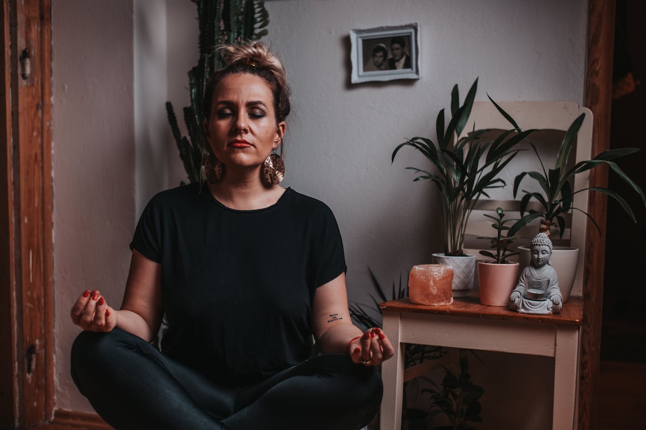 Calm woman in a black t-shirt and black pants meditating with closed eyes at home