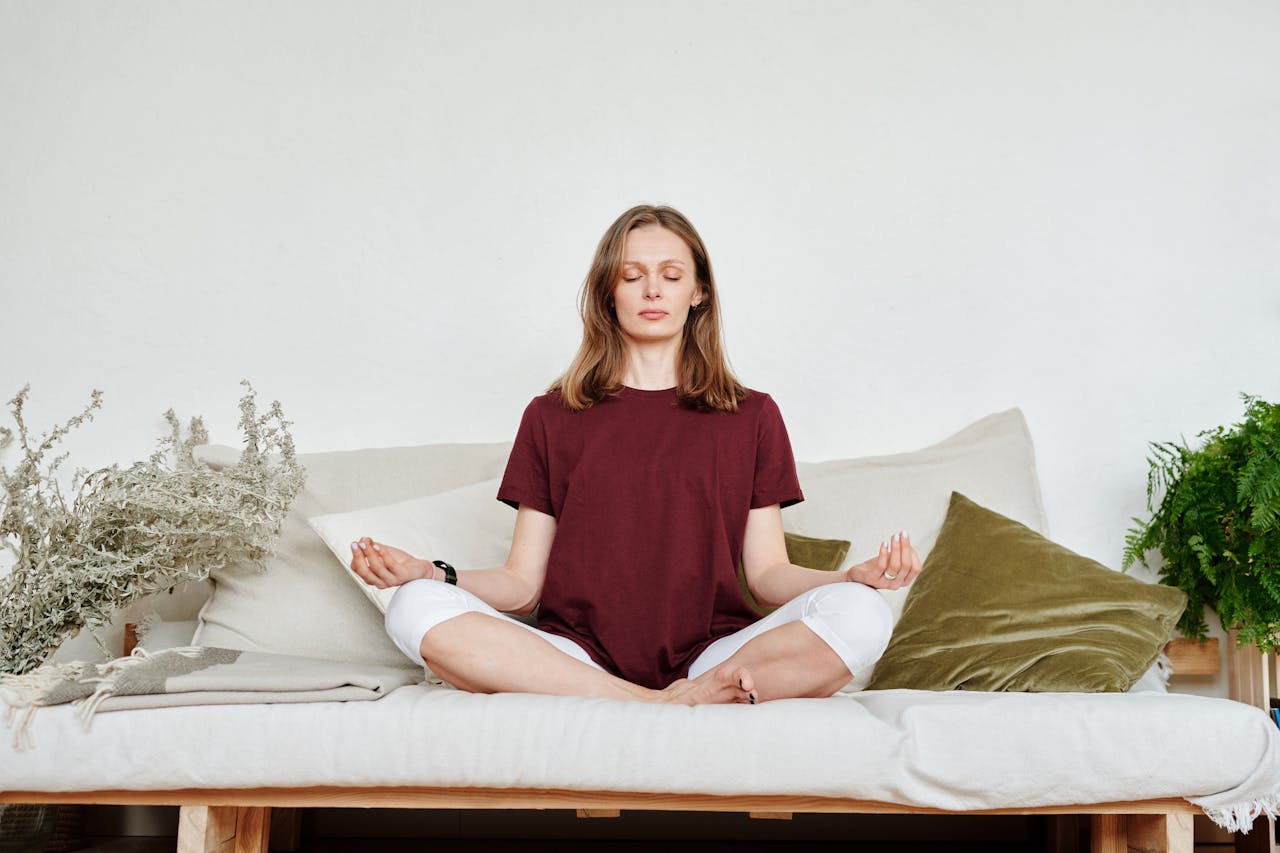Photo of Woman in a red t-shirt and white pants Sitting on Couch Meditating