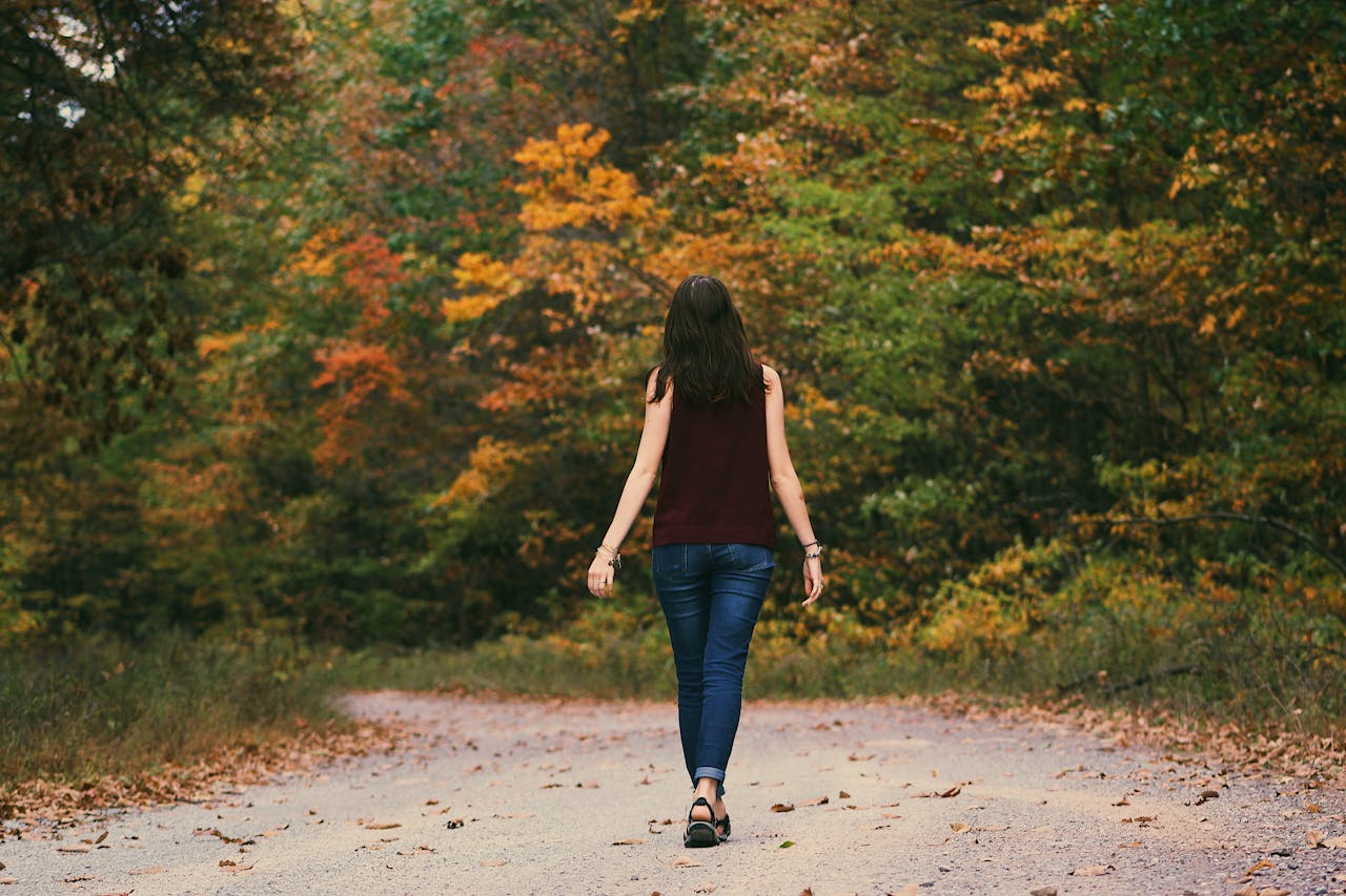 Woman in Brown Sleeveless Dress and Blue Jeans Standing on Gray Path Road,