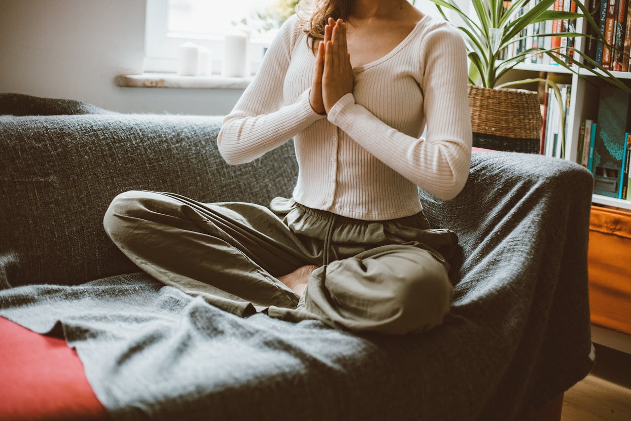 Photo of  Woman in a white shirt and green pants Sitting on Sofa Meditating