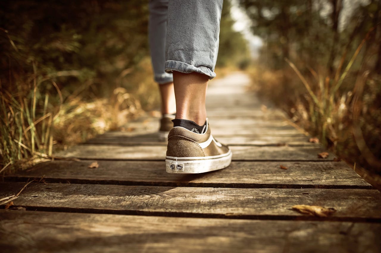 Person wearing a brown sneakers and blue jeans Stands on Brown Pathway