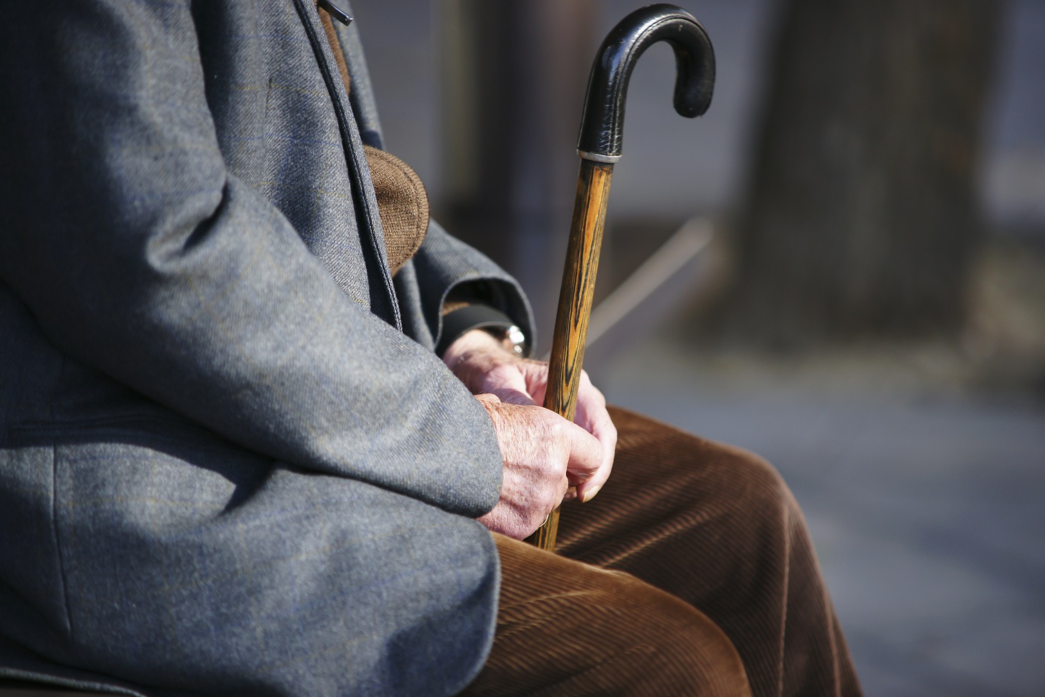 Senior man with a cane sitting on wooden bench in a park.