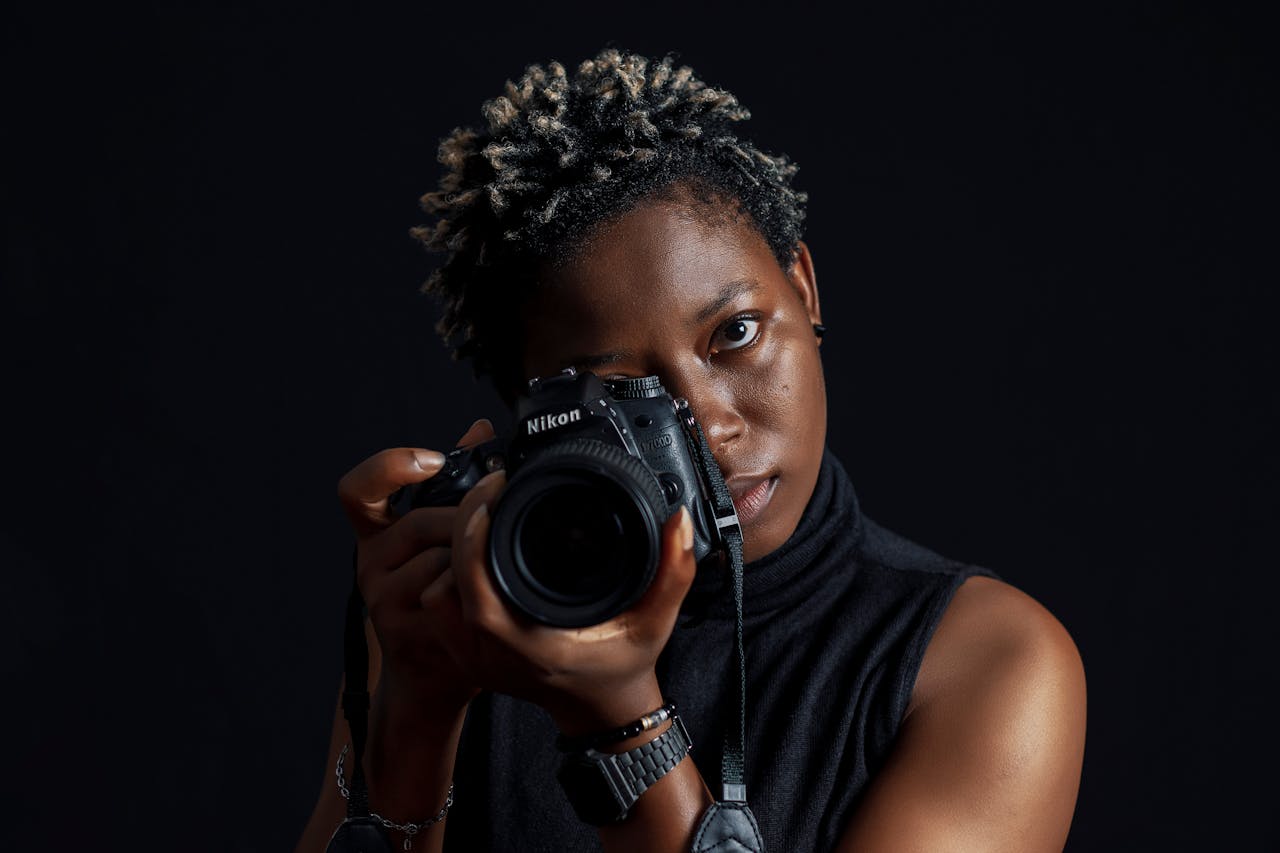 A Woman with Short Hair Holding a Digital Camera on Black Background.