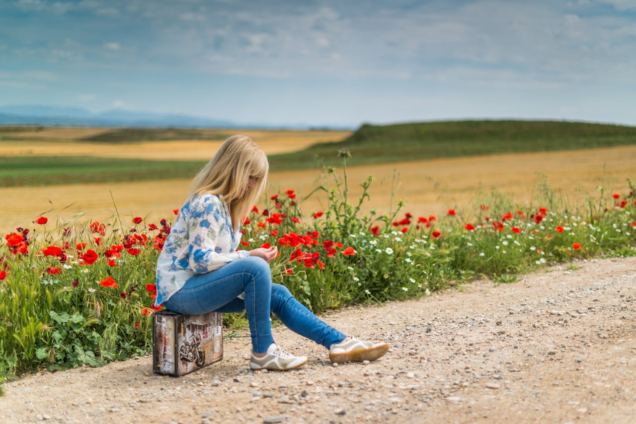 Girl seating on the road on suitcase with flowers.