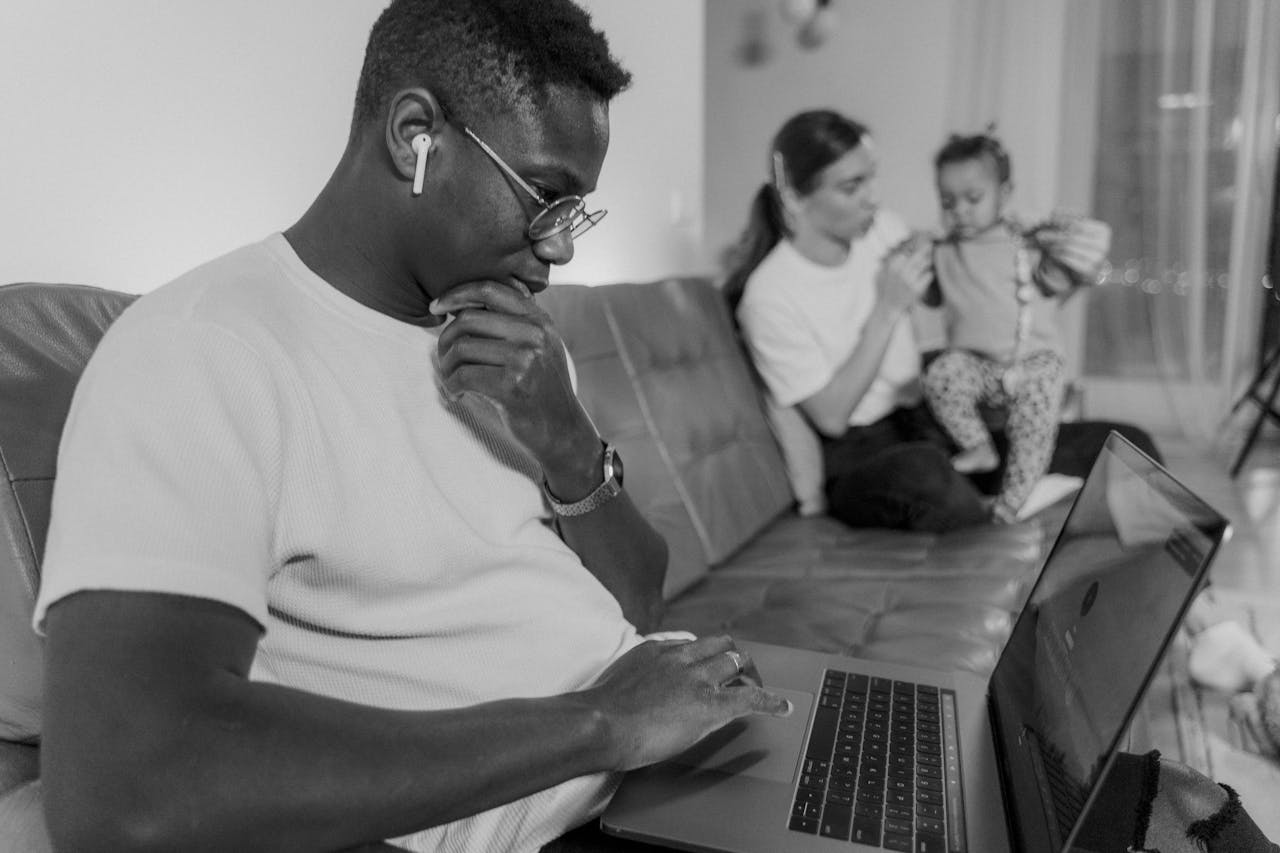 Man Using Laptop Sitting on Couch Near a Woman Holding Holding a Baby