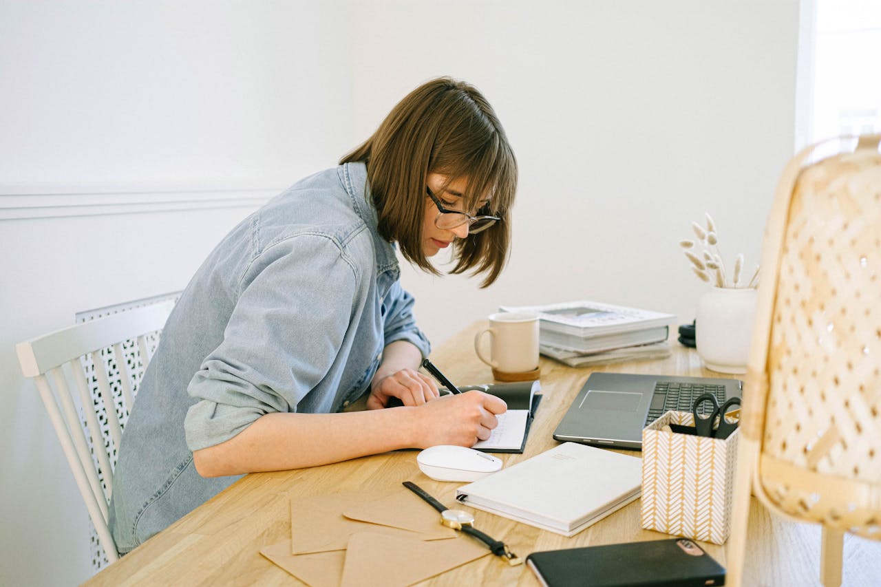 Portrait Photo of a Woman sitting on a desk and Writing on a Notebook