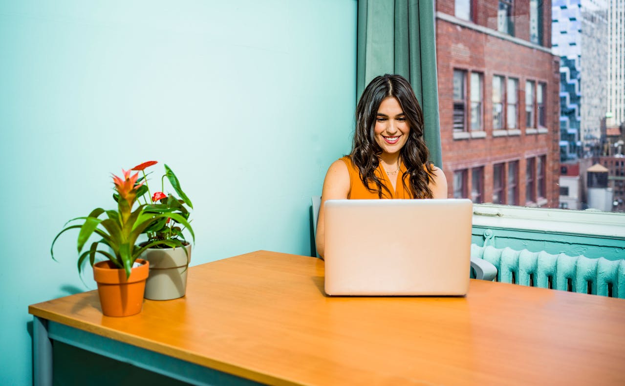 Portrait Photo of a Woman in a yellow shirt Using Laptop placed on a wooden table and smiling