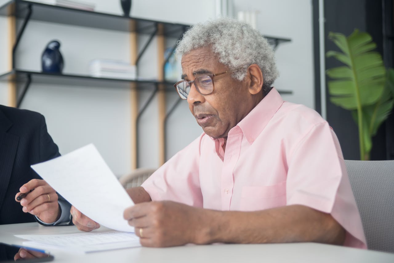 A Man in Pink Button-Up Shirt Reading a Document in an office sitting next to other man