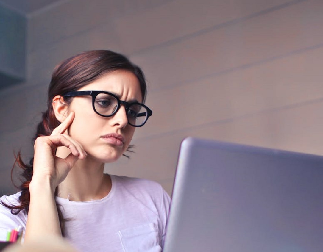 Woman with glasses reading on laptop.