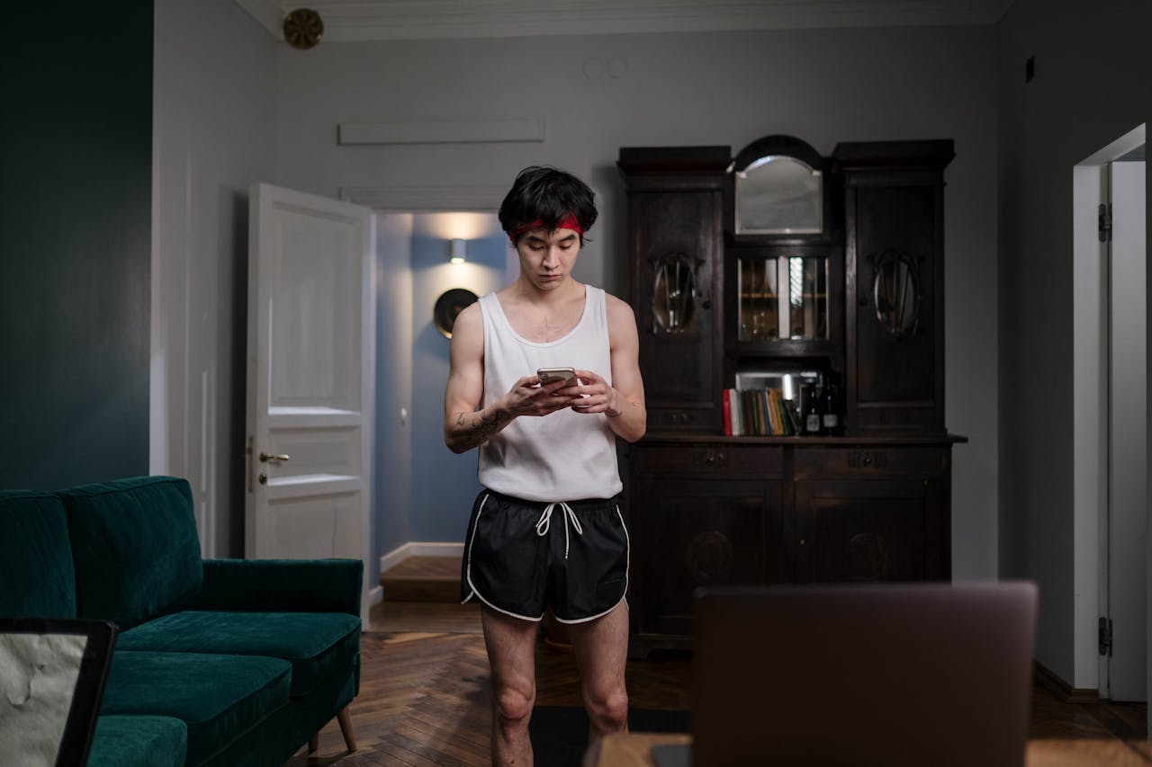 Man in White Tank Top and Black Shorts looking at phone.