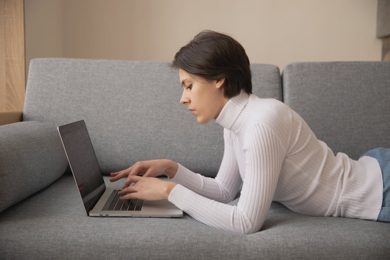 Photo Of Woman Laying On Sofa with her laptop.