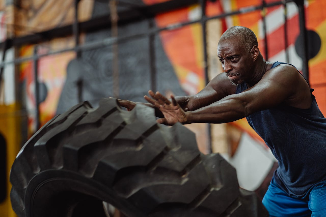 Man in Blue Tank Top Pushing a Tire