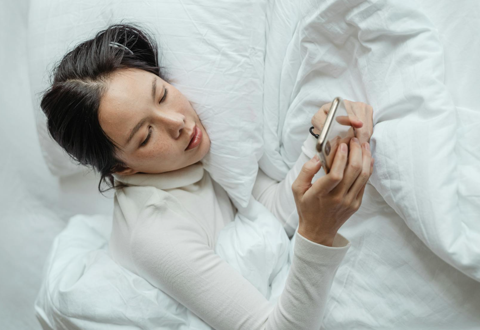 woman waking up and using smartphone in bed
