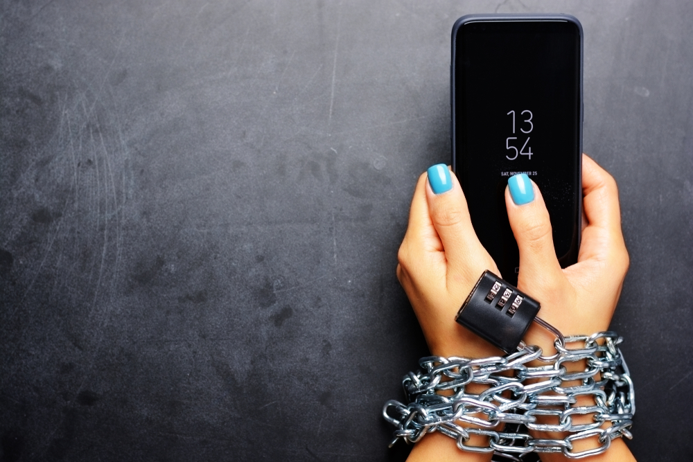 Woman hands tied with metallic chain holding phone