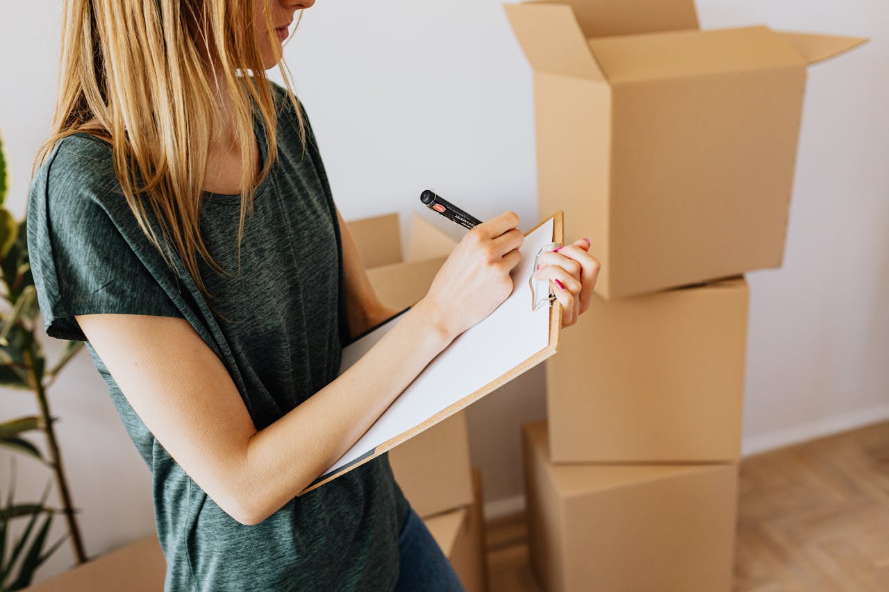 woman taking notes in clipboard near carton boxes