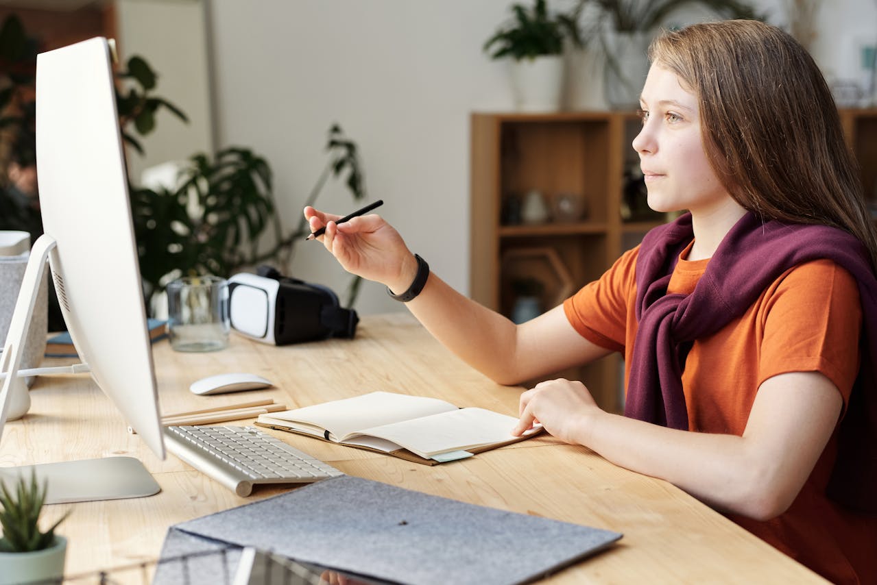 Girl Holding Pencil While Looking at monitor.