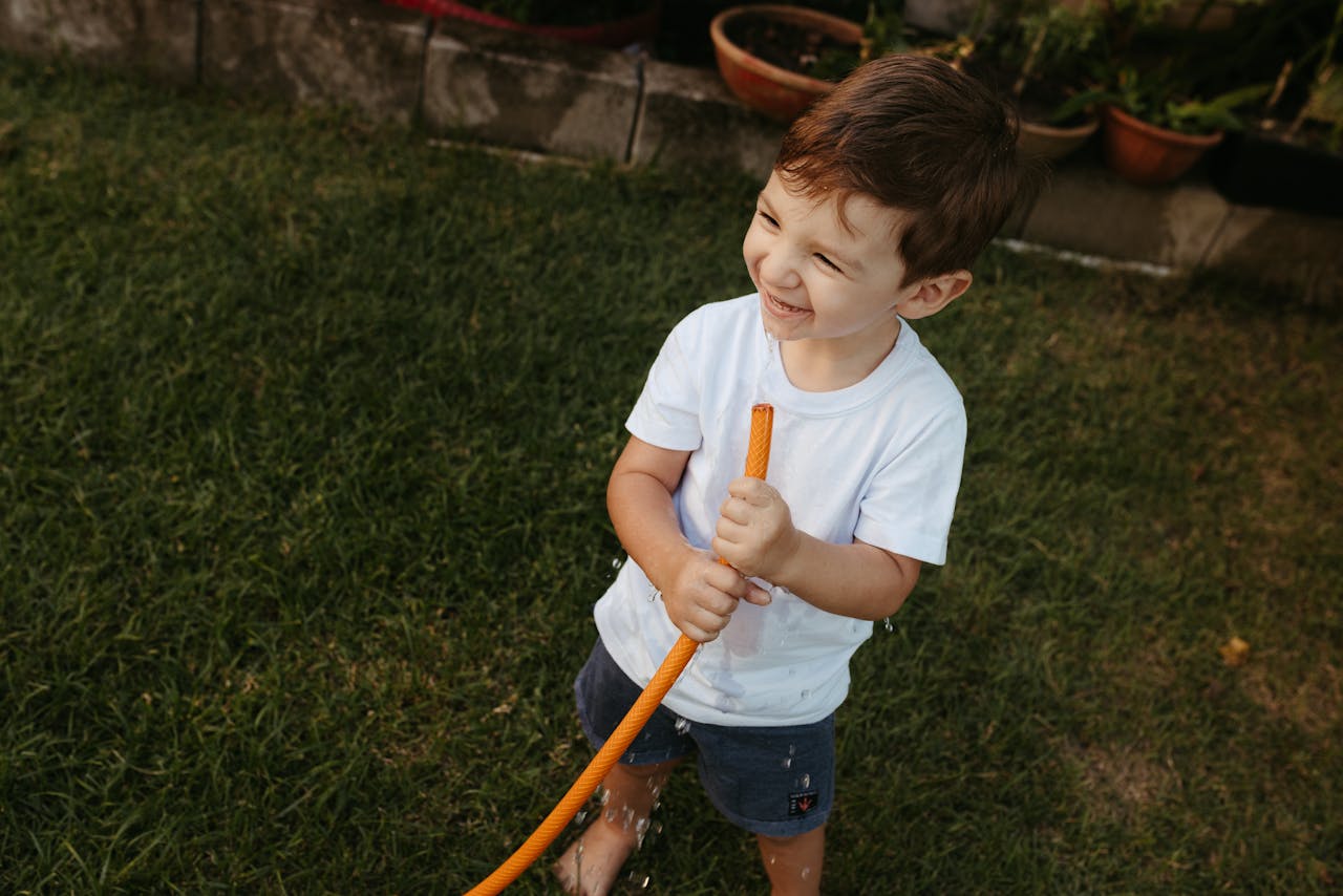 Boy in White T-Shirt Standing with Hose in Garden