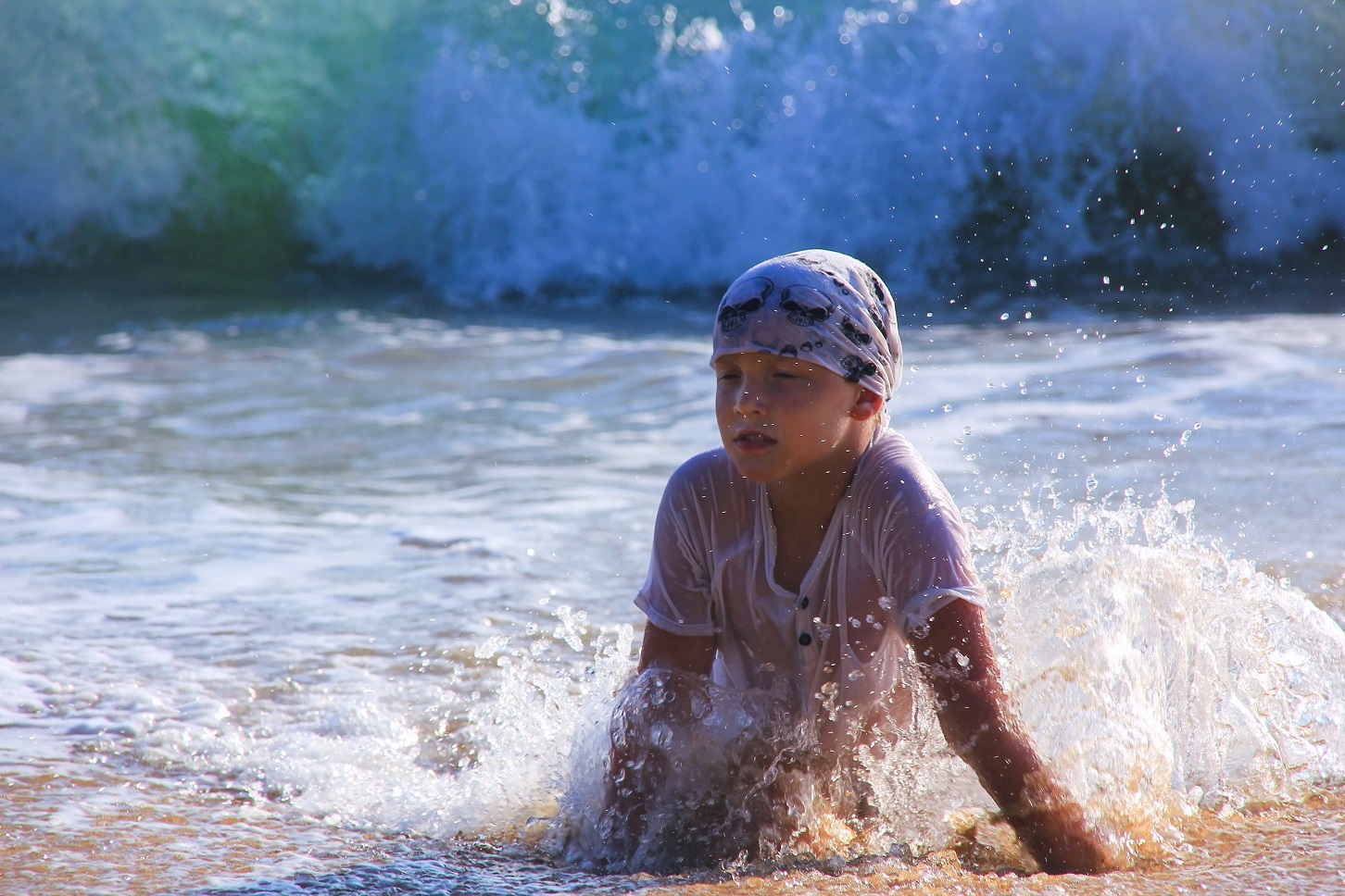 Boy wearing wet t-shirt is playing and having fun on beach.
