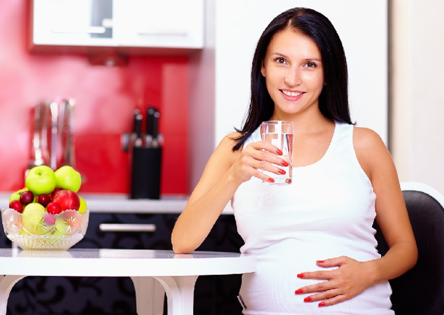 Pregnant woman drinking water in kitchen