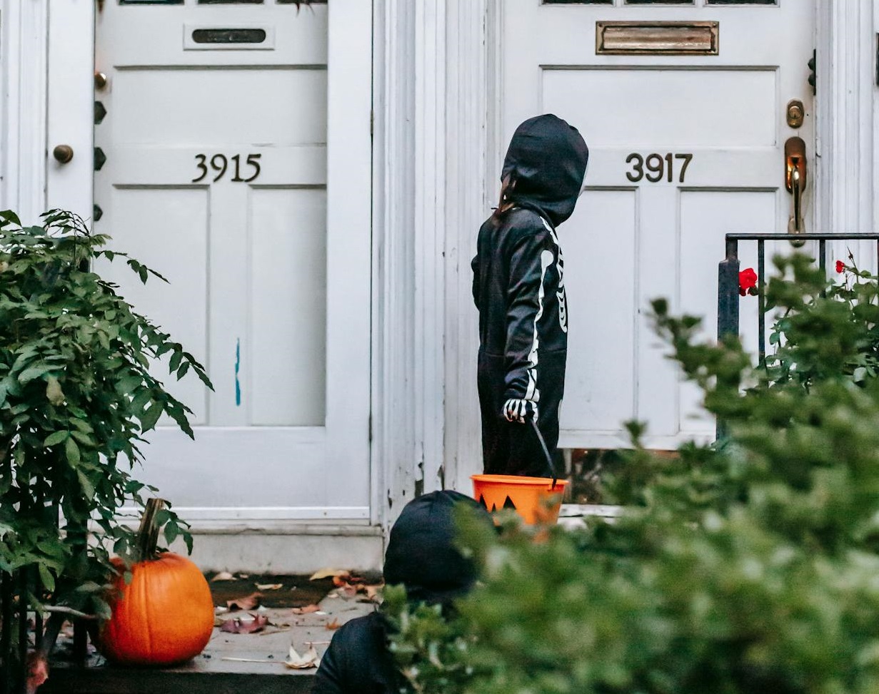 Children in skeleton costumes knocking on white door on Halloween.