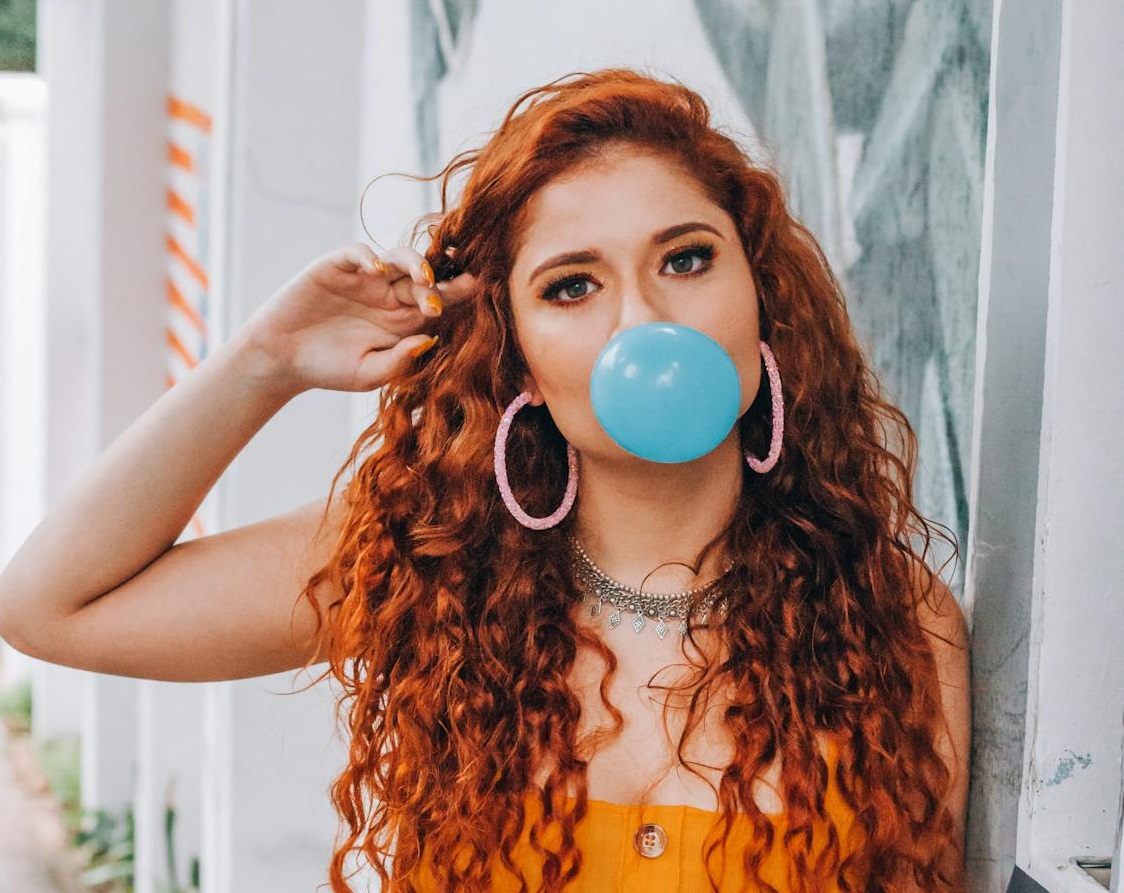 Brown hair woman with blue bubblegum in her mouth.