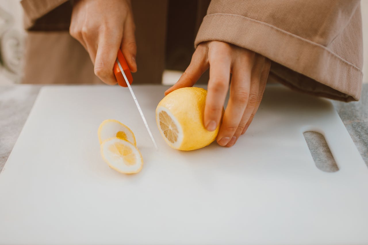 A Person Cutting Lemon on plastic cutting board.