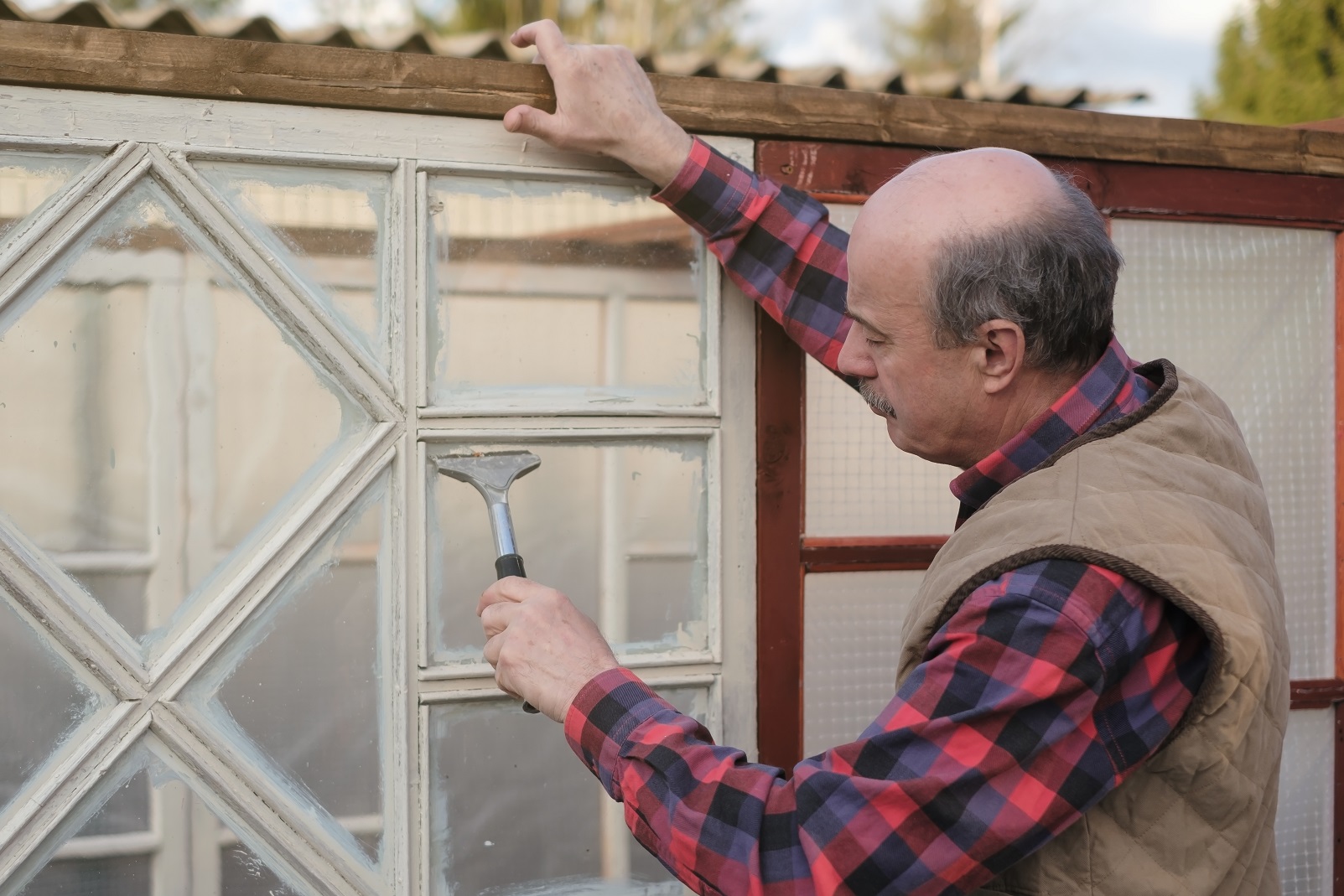 Senior bald man farmer cleans the window from the paint.