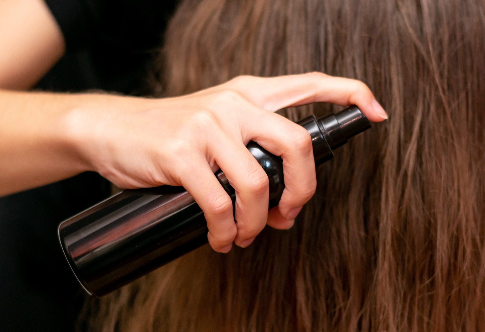 Young woman hand holds bottle and spraying her wavy blond long hair.