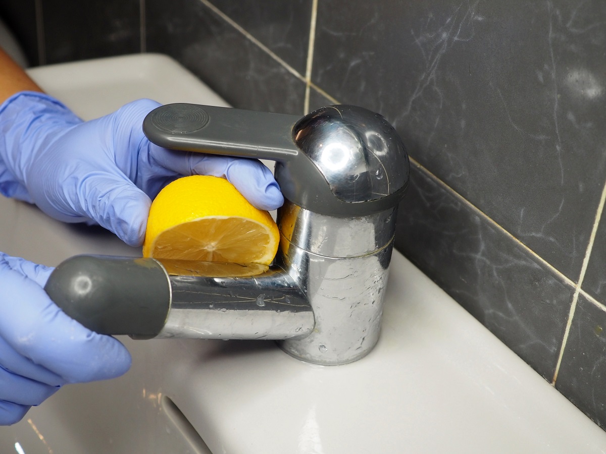 The chrome faucet of the sink in the bathroom is cleaned of limescale with a lemon.