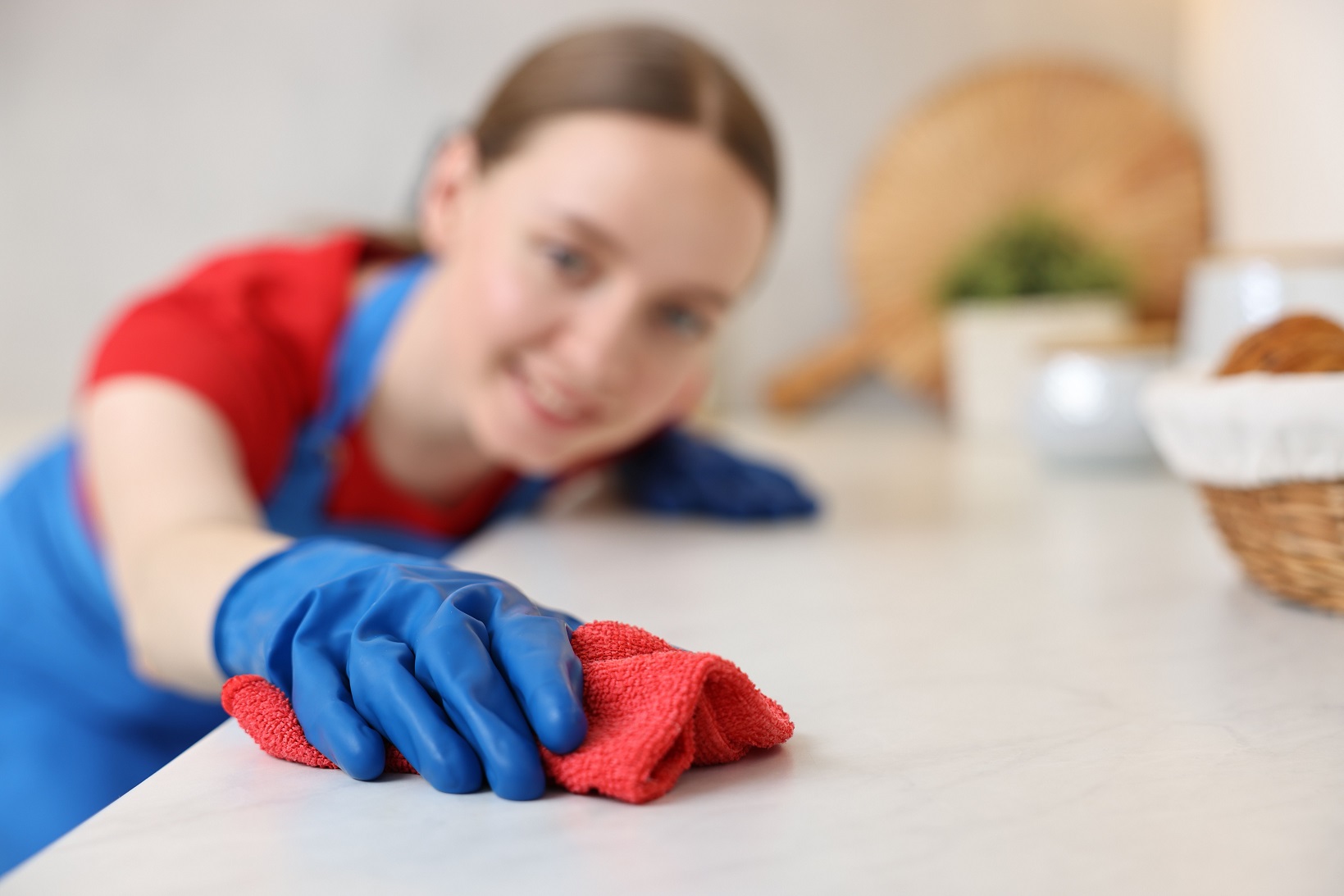 Woman cleaning white countertop with rag in kitchen, selective focus.
